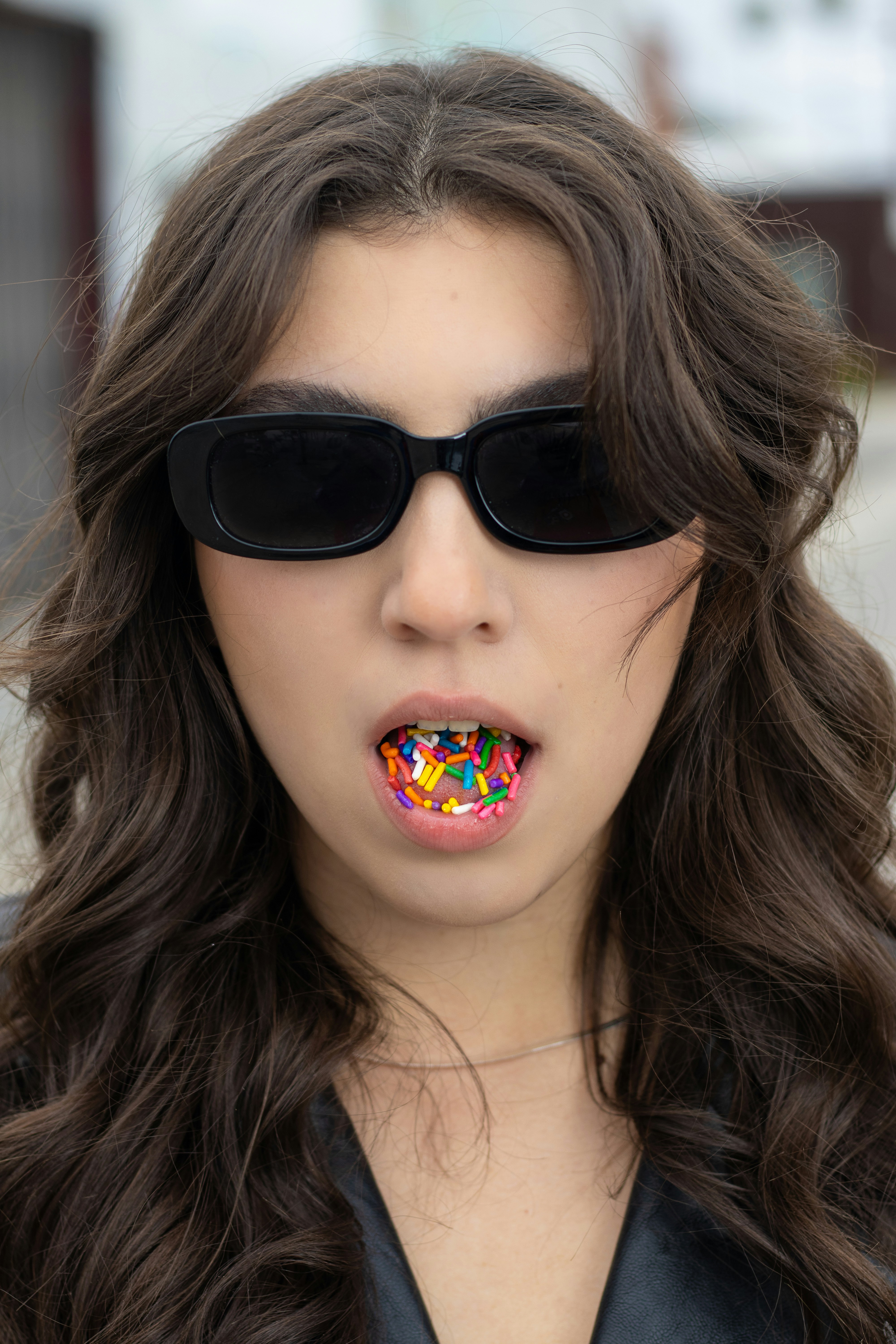 Girl with curly hair, wearing black sunglasses, and sticking our tongue with sprinkles.